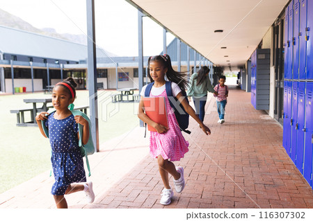 In school corridor outdoors, a biracial teacher walks behind her daughters and son, with copy space 116307302