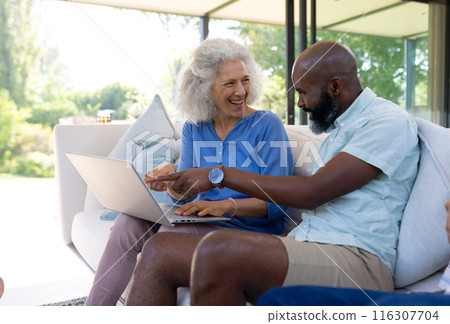 At home, diverse senior friends laughing while viewing laptop 116307704