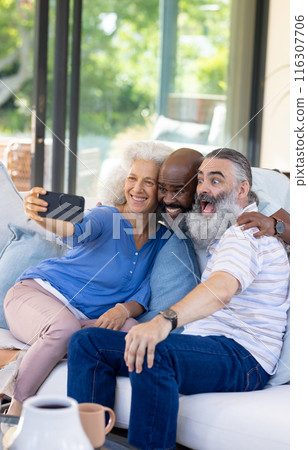 Diverse senior friends taking joyful couch selfie at home 116307706