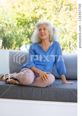 Outdoors, Caucasian senior woman wearing blue shirt, sitting on gray sofa 116307709