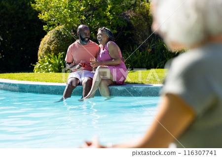 Outdoors, diverse senior friends, laughing by pool, holding drinks Outdoors, diverse senior friends, laughing by pool, holding drinks 116307741