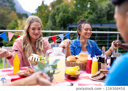 Happy diverse group of friends praying and having dinner at balcony with flags of usa 116308458