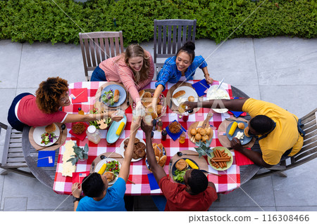 Happy diverse group of friends cheering with drinks and having dinner at balcony with flags of usa 116308466