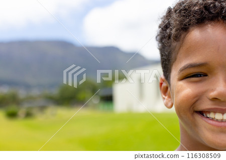 A biracial boy with curly hair smiles outside, copy space 116308509