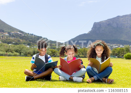 Biracial children are engrossed in reading books outdoors with copy space 116308515