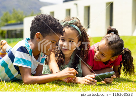 Biracial boy and girls are lying on the grass, looking at a smartphone together Biracial boy and girls are lying on the grass, looking at a smartphone together 116308528