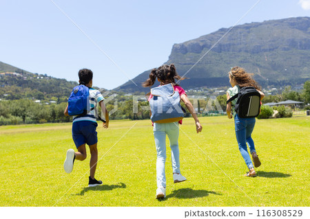 Three children are running joyfully across a grassy field on a sunny day 116308529