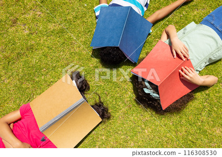 Three children are lying on grass reading books, with a focus on education and leisure Three children are lying on grass reading books, with a focus on education and leisure 116308530