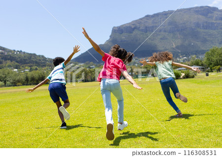 Three biracial children run joyfully across grassy field 116308531