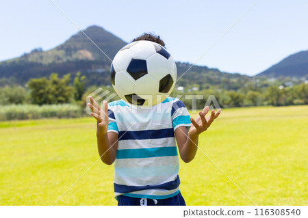 Biracial boy plays with a soccer ball outdoors, surrounded by greenery and mountains 116308540