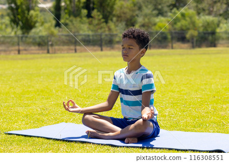 Biracial boy meditates on a yoga mat in a sunny park Biracial boy meditates on a yoga mat in a sunny park 116308551