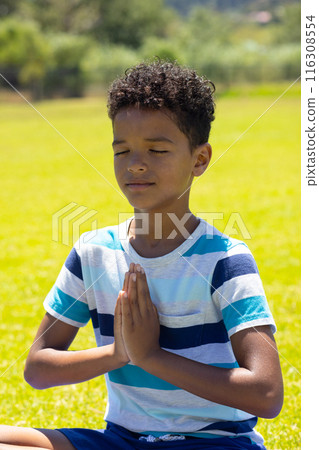 Biracial boy meditates with hands pressed together in a peaceful outdoor setting 116308554