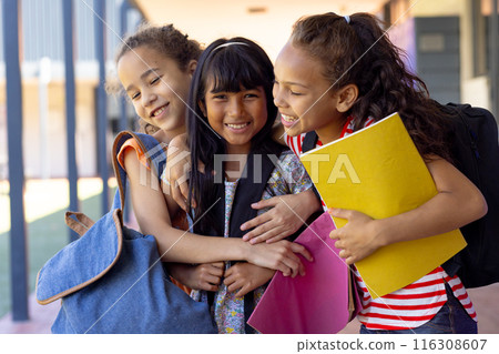 Three biracial girls are embracing outside a school, smiling with notebooks in hand Three biracial girls are embracing outside a school, smiling with notebooks in hand 116308607