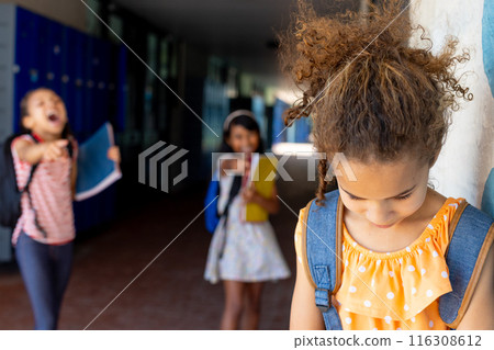 In school, three biracial female students are in the hallway, experiencing bullying 116308612