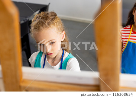 In school, during art class, a Caucasian girl with blonde hair is focusing on her work 116308634