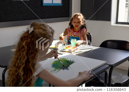 Caucasian and biracial girls are painting in a sunlit room at school Caucasian and biracial girls are painting in a sunlit room at school 116308643