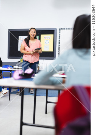 In school, biracial young female teacher teaching in classroom, young girl listening In school, biracial young female teacher teaching in classroom, young girl listening 116308644