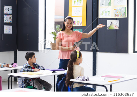 A young biracial female teacher points at posters, holding tablet, in a pink top 116308657