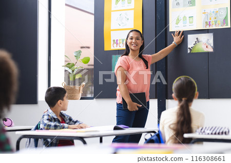 A biracial young female teacher instructs attentive students in a classroom 116308661