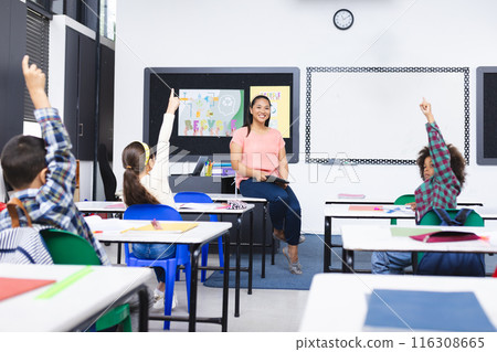 In school, young biracial female teacher smiles at students raising hands in class 116308665