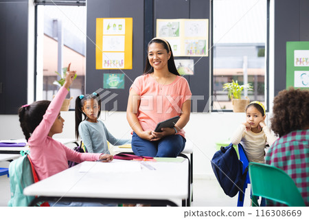 Biracial female teacher with 4 students raising their hands to ask questions in class 116308669