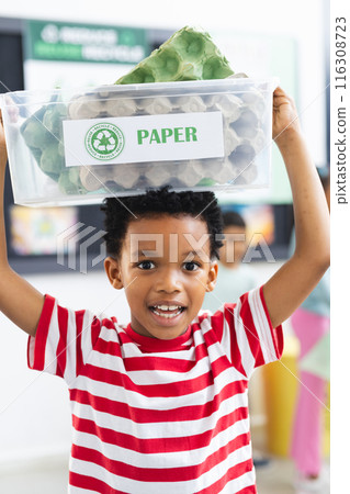 Young African American boy holds recycle bin above his head in classroom at school Young African American boy holds recycle bin above his head in classroom at school 116308723