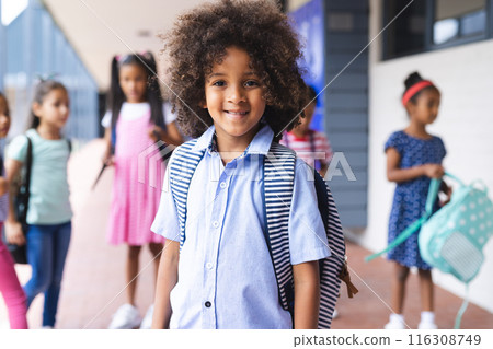 In school, outdoors, young biracial girl with curly hair is standing, smiling 116308749