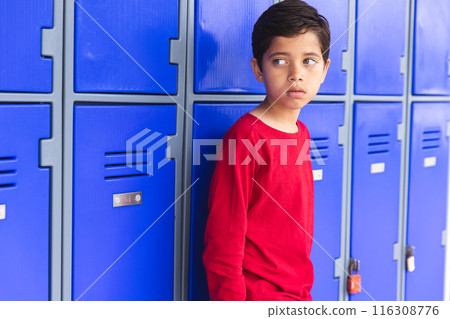 In school, young biracial male student leaning against blue lockers outdoors 116308776