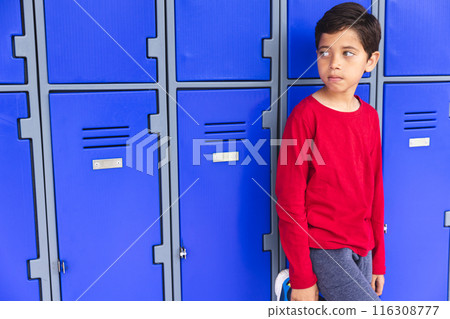 In school, a young biracial boy standing by blue lockers outdoors, looking away, with copy space 116308777