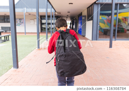In school, young biracial male student wearing a red hoodie and jeans walking outdoors 116308784