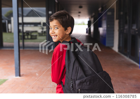 In school, young biracial male student wearing a red shirt is walking outdoors 116308785