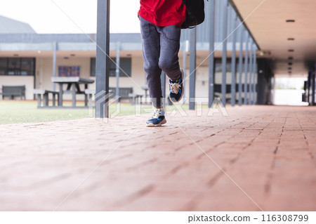 In school, young biracial male student wearing sneakers is walking outdoors 116308799