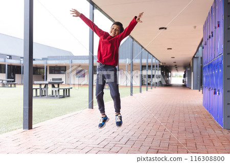 In school, outdoors, a biracial young boy is jumping with joy 116308800