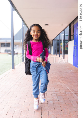 In school, young biracial female student holding a notebook walking outdoors 116308819