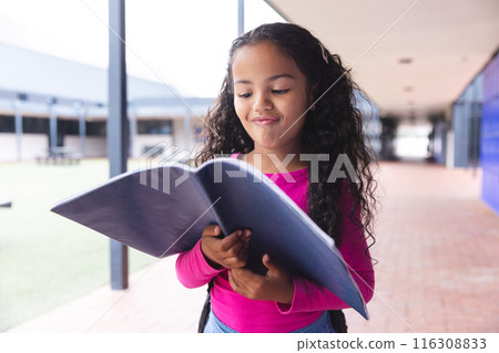 In school, young biracial girl with long curly hair is reading a book outdoors In school, young biracial girl with long curly hair is reading a book outdoors 116308833