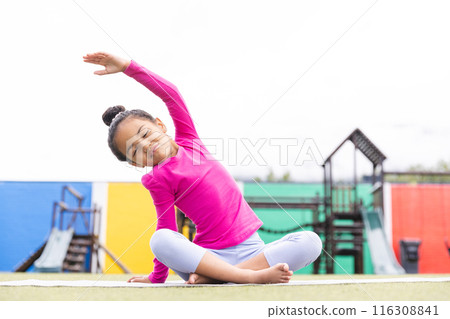 In school, young biracial girl stretching on a mat outdoors doing yoga 116308841