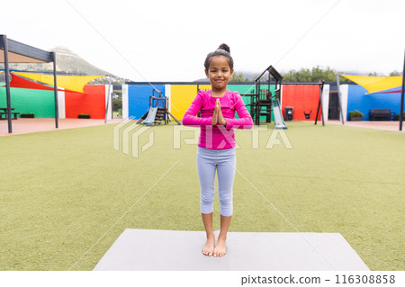 In school playground outdoors, a biracial young girl is practicing yoga 116308858