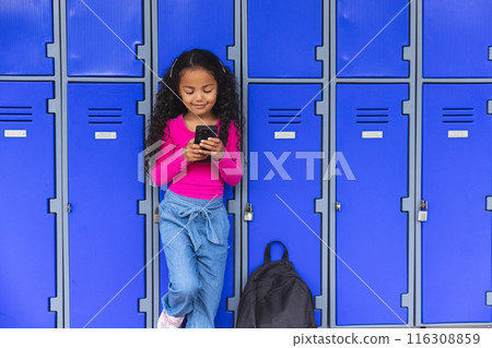 In school, young biracial girl is looking at a smartphone, copy space In school, young biracial girl is looking at a smartphone, copy space 116308859