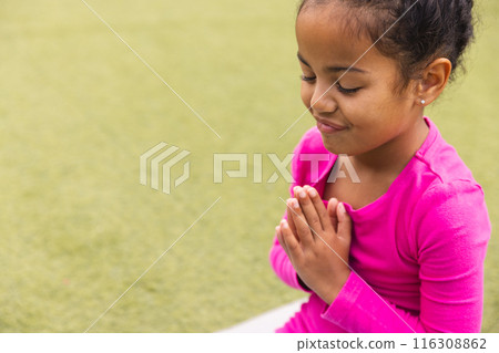 Young biracial girl in pink prays and does yoga on green grass at school with c Young biracial girl in pink prays and does yoga on green grass at school with c 116308862