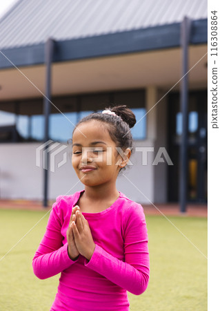 In school, young biracial girl wearing pink is standing with hands together outdoors doing yoga In school, young biracial girl wearing pink is standing with hands together outdoors doing yoga 116308864