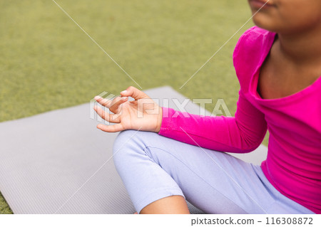 A young biracial girl wearing pink is practicing yoga outdoors with copy space 116308872