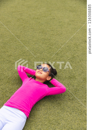 In school, outdoors, biracial young girl wearing sunglasses lying on grass with copy space 116308885