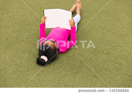 In school, biracial girl lying on grass outdoors reading book In school, biracial girl lying on grass outdoors reading book 116308888