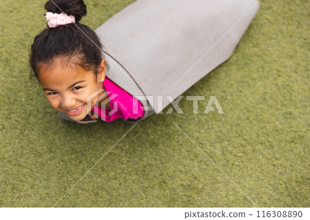 In school, outdoors, a biracial young girl wearing pink is lying on her stomach 116308890