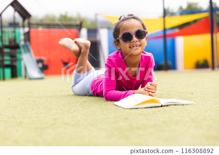 In school, outdoors, a biracial young girl wearing sunglasses is reading 116308892