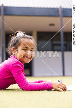 In school, outdoors, a biracial young girl wearing pink is writing on paper with copy space In school, outdoors, a biracial young girl wearing pink is writing on paper with copy space 116308893