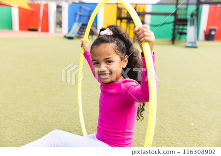 In school outdoors, biracial young girl is playing with a yellow hula hoop In school outdoors, biracial young girl is playing with a yellow hula hoop 116308902