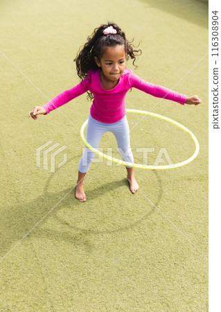 In school, outdoors, a biracial young girl is playing with a yellow hula hoop In school, outdoors, a biracial young girl is playing with a yellow hula hoop 116308904