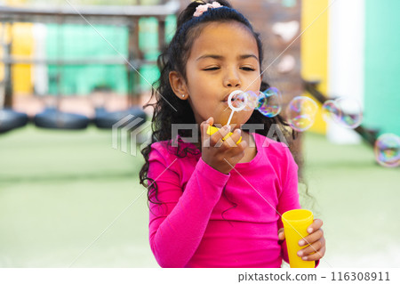 In school outdoors, young biracial girl is blowing bubbles In school outdoors, young biracial girl is blowing bubbles 116308911
