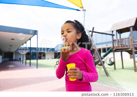 In school playground outdoors, biracial young girl blowing bubbles 116308913